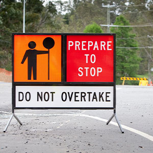 A man stands in front of a road sign that instructs drivers to "Prepare to Stop," emphasizing road safety.