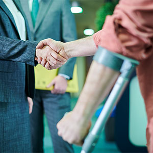 A lawyer in a suit shaking hands with a client on crutches, representing legal support for an injury claim