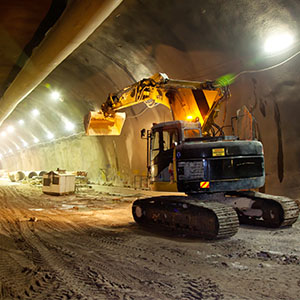 Heavy machinery operates in a well-lit underground tunnel under construction. 
