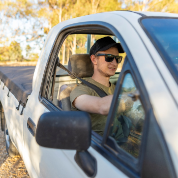 A man wearing a hat and sunglasses driving a Ford ute vehicle