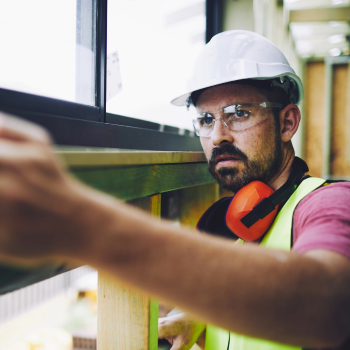 A construction worker wearing personal protective equipment measuring a window frame